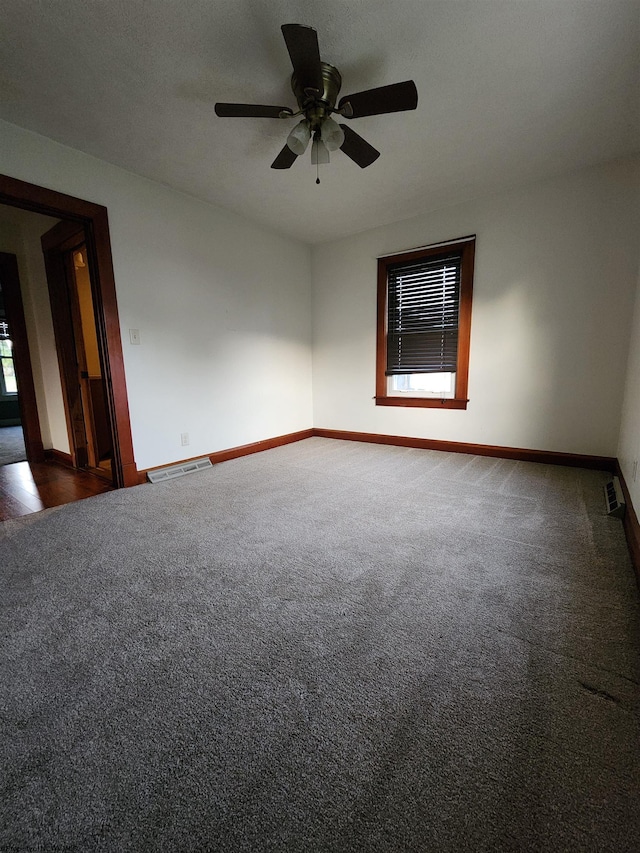 empty room with ceiling fan, plenty of natural light, and dark colored carpet