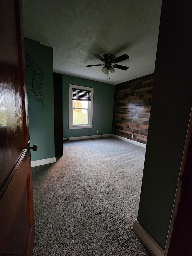 unfurnished room with a textured ceiling, carpet flooring, wooden walls, and ceiling fan