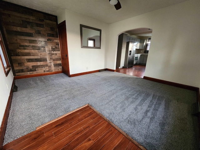 unfurnished living room with wood walls, dark hardwood / wood-style floors, and ceiling fan