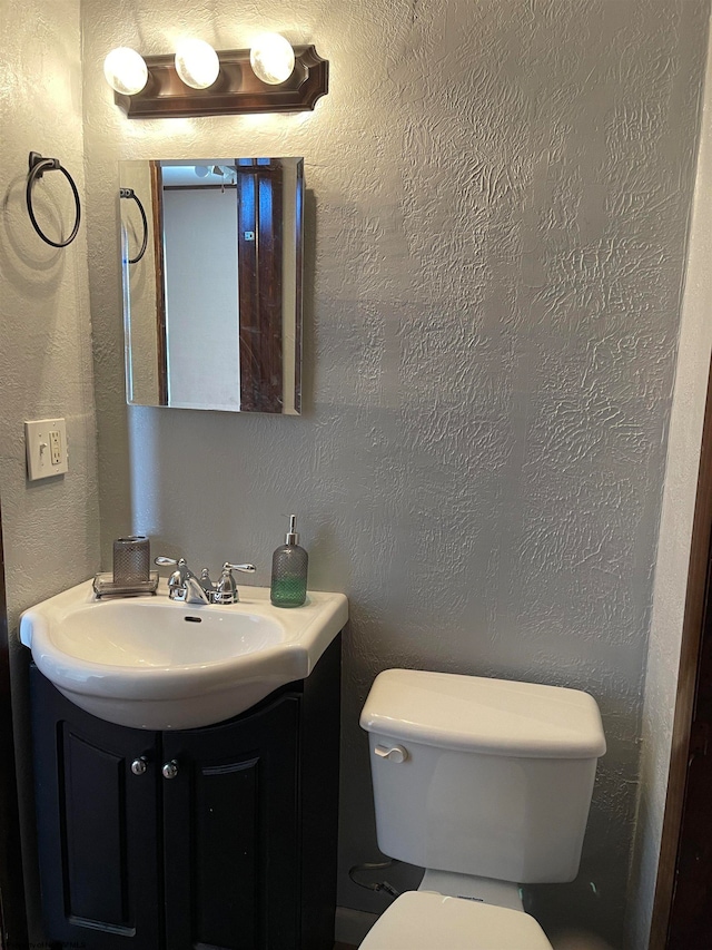 bathroom with a textured wall, vanity, and toilet