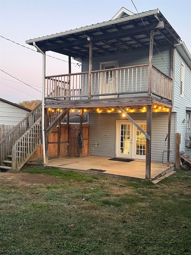 back house at dusk with a wooden deck, a patio, and a lawn