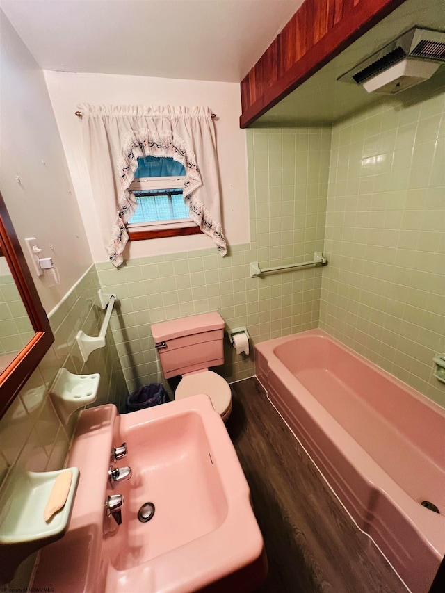 bathroom featuring toilet, tile walls, hardwood / wood-style floors, and a bath