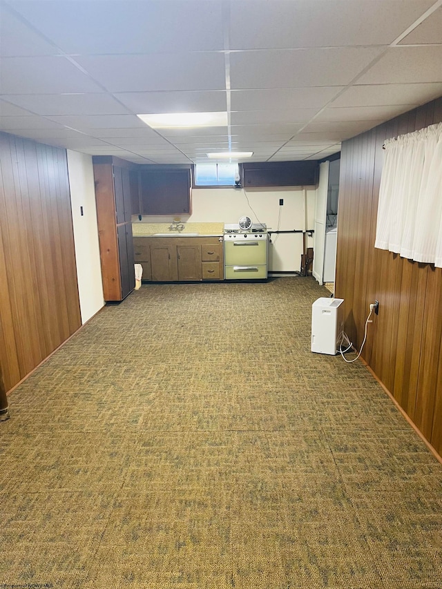 basement with sink, wood walls, a drop ceiling, and dark colored carpet