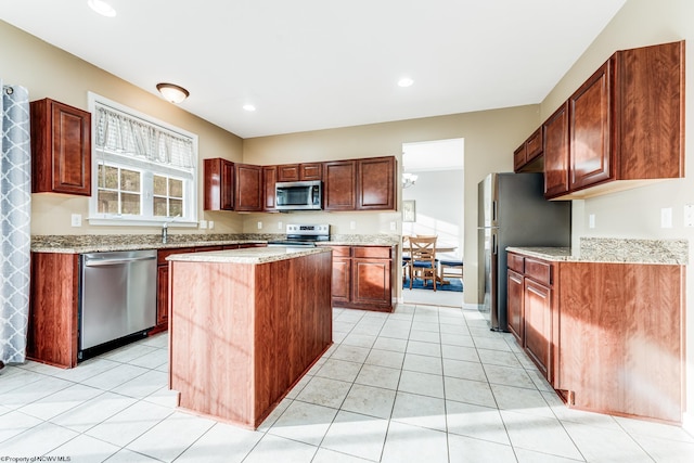 kitchen with appliances with stainless steel finishes, light stone countertops, light tile patterned flooring, and a kitchen island