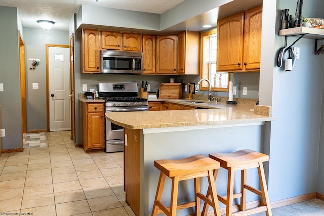 kitchen featuring kitchen peninsula, stainless steel appliances, sink, a breakfast bar, and light tile patterned floors