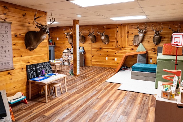 game room featuring a drop ceiling, wooden walls, and hardwood / wood-style floors