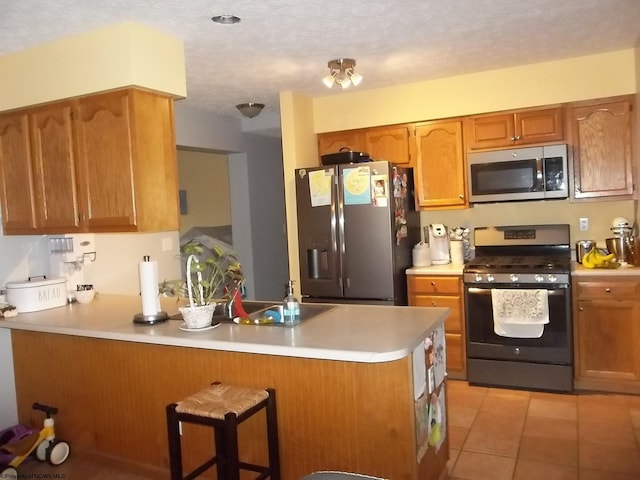 kitchen with a breakfast bar area, kitchen peninsula, light tile patterned flooring, appliances with stainless steel finishes, and a textured ceiling