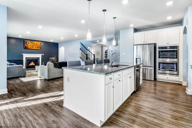 kitchen featuring appliances with stainless steel finishes, sink, white cabinetry, dark stone counters, and a kitchen island with sink