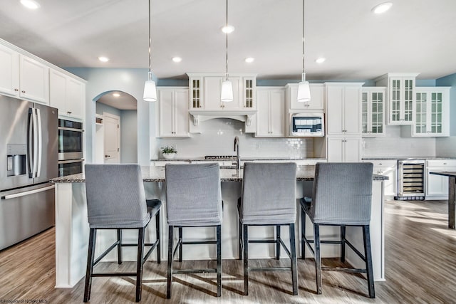 kitchen with a center island with sink, wine cooler, hanging light fixtures, and stainless steel appliances