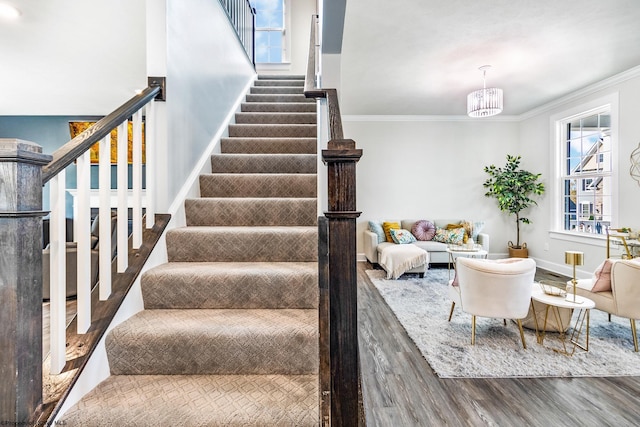 stairway with ornamental molding, wood-type flooring, and an inviting chandelier