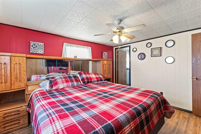 bedroom featuring ceiling fan, hardwood / wood-style flooring, and wooden walls