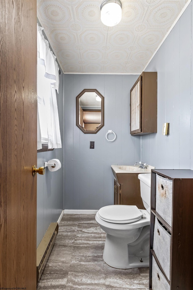 bathroom featuring a baseboard heating unit, wood-type flooring, toilet, wood walls, and vanity