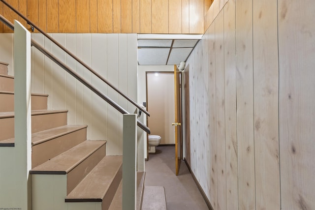 staircase with concrete floors and wood walls