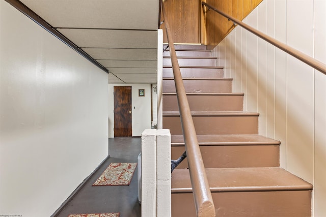 staircase featuring concrete floors and wood walls