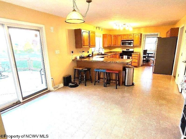 kitchen with kitchen peninsula, appliances with stainless steel finishes, a textured ceiling, hanging light fixtures, and a breakfast bar area