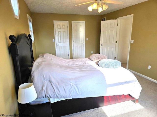 carpeted bedroom with multiple closets, ceiling fan, and a textured ceiling