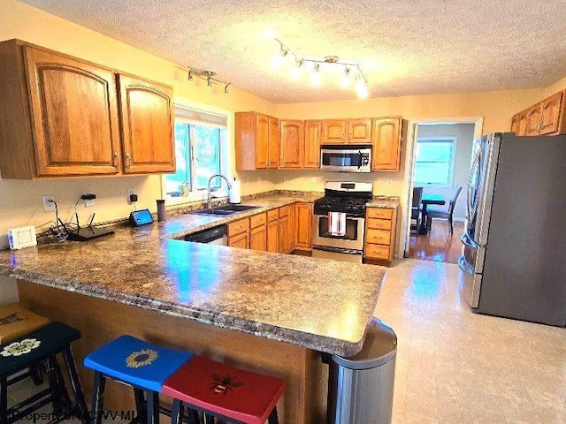 kitchen with sink, kitchen peninsula, a textured ceiling, a kitchen bar, and appliances with stainless steel finishes