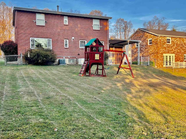 rear view of property featuring central AC, a lawn, and a playground