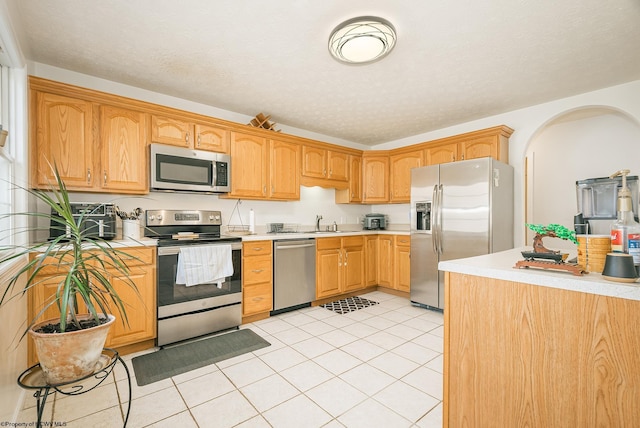 kitchen with a textured ceiling, stainless steel appliances, light tile patterned floors, and sink