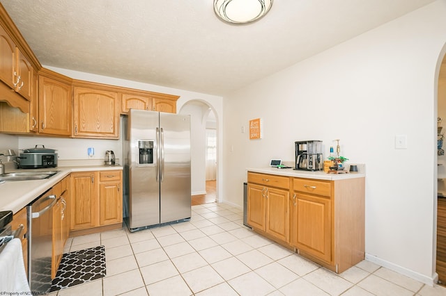 kitchen with a textured ceiling, sink, light tile patterned flooring, and stainless steel appliances