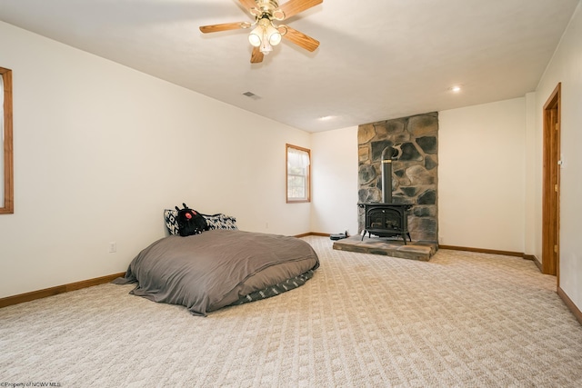 carpeted bedroom with ceiling fan and a wood stove