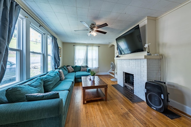 living room with a fireplace, ceiling fan, wood-type flooring, and crown molding