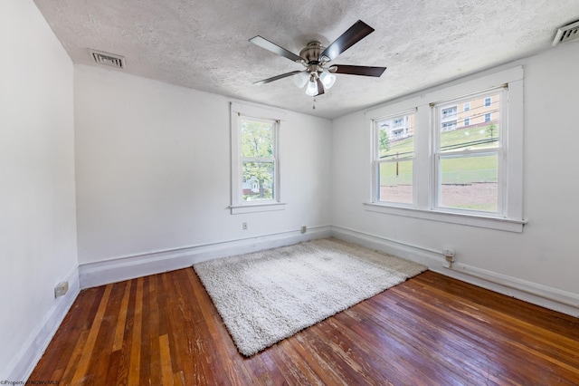 empty room featuring ceiling fan, a wealth of natural light, a textured ceiling, and dark hardwood / wood-style floors