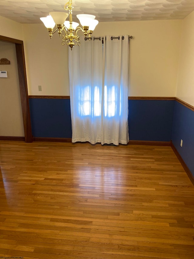 spare room featuring hardwood / wood-style floors, a chandelier, and a textured ceiling