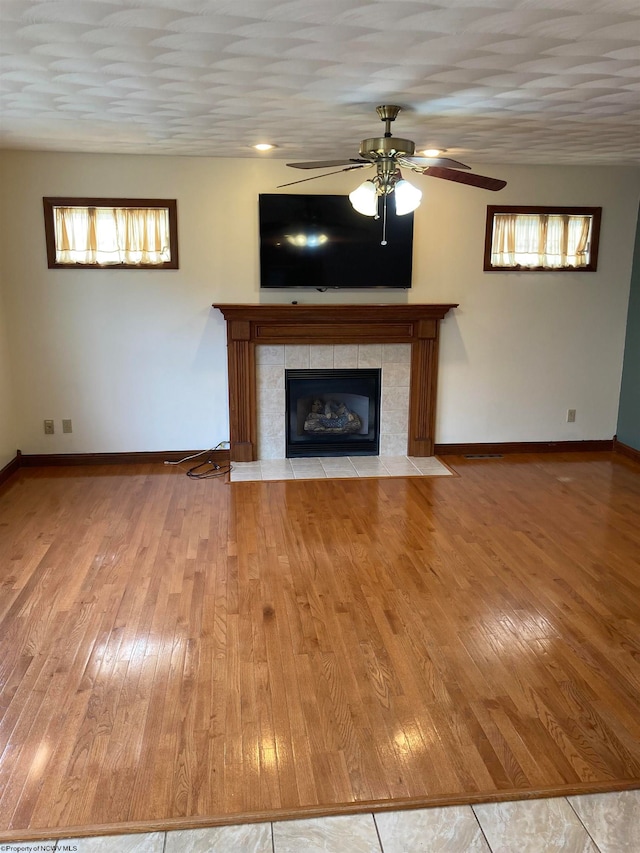 unfurnished living room featuring hardwood / wood-style floors, ceiling fan, plenty of natural light, and a tile fireplace