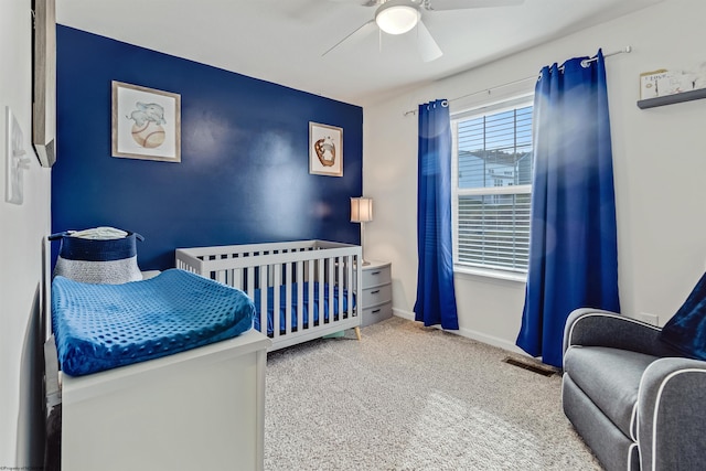 bedroom with a crib, ceiling fan, and carpet flooring