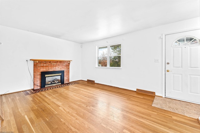 unfurnished living room featuring hardwood / wood-style floors and a brick fireplace