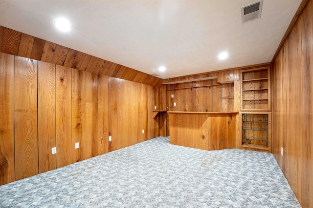 carpeted spare room with wood walls and bar area