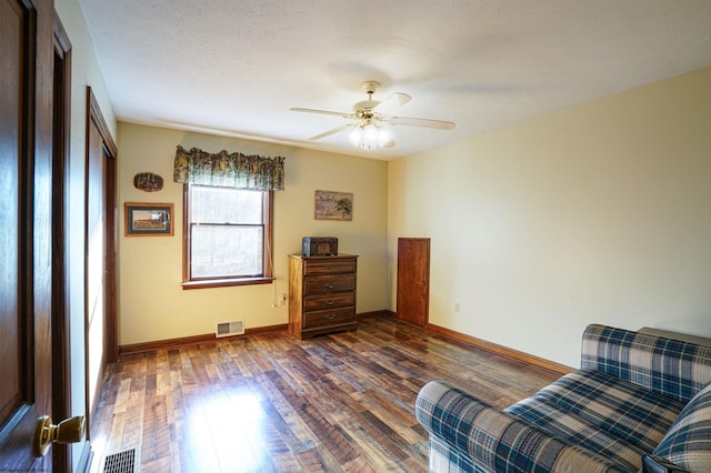 living area with a textured ceiling, dark wood-type flooring, and ceiling fan