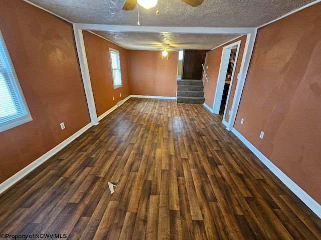 empty room with dark hardwood / wood-style flooring, a wealth of natural light, a textured ceiling, and ceiling fan