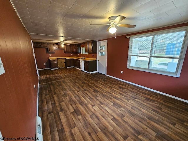 unfurnished living room featuring wood walls, ceiling fan, sink, and dark hardwood / wood-style floors