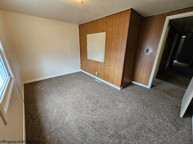 unfurnished bedroom with wooden walls, a closet, and dark carpet