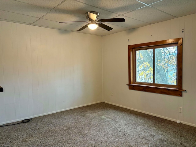 carpeted empty room featuring wood walls, a paneled ceiling, and ceiling fan