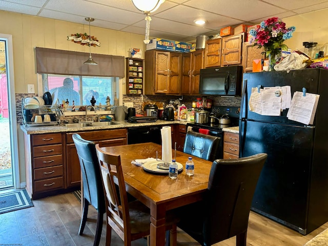 kitchen with black appliances, a paneled ceiling, pendant lighting, sink, and light hardwood / wood-style flooring