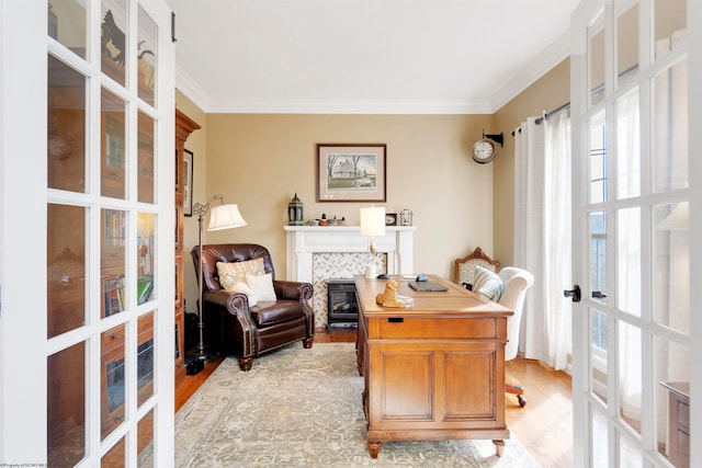 home office featuring light wood-type flooring, a tiled fireplace, french doors, and crown molding