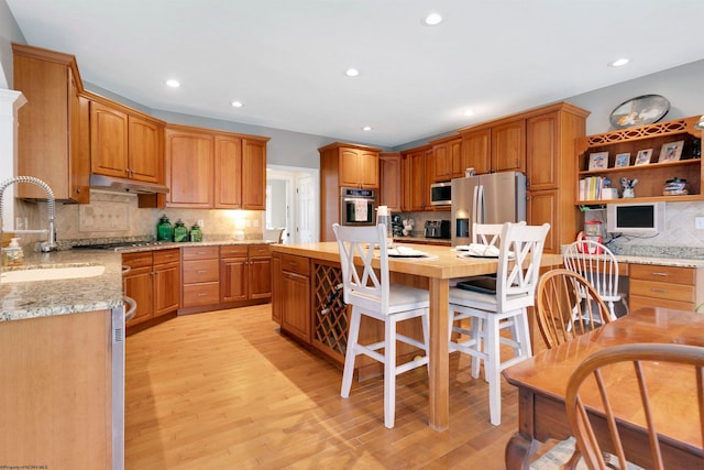 kitchen with light stone counters, appliances with stainless steel finishes, decorative backsplash, sink, and light hardwood / wood-style floors