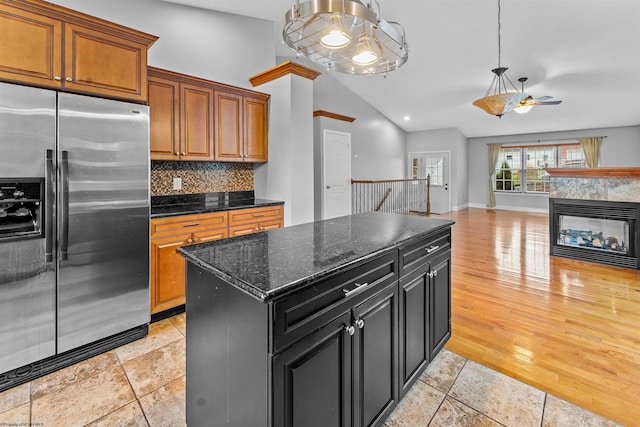 kitchen with stainless steel refrigerator with ice dispenser, dark stone countertops, backsplash, lofted ceiling, and a center island