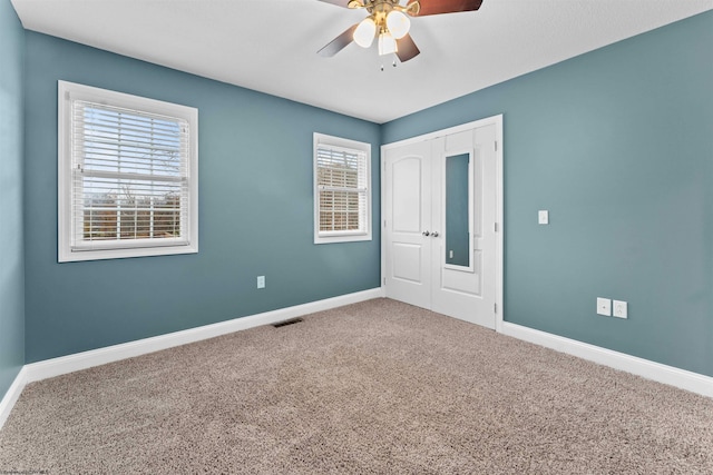 unfurnished bedroom with a closet, multiple windows, ceiling fan, and carpet floors