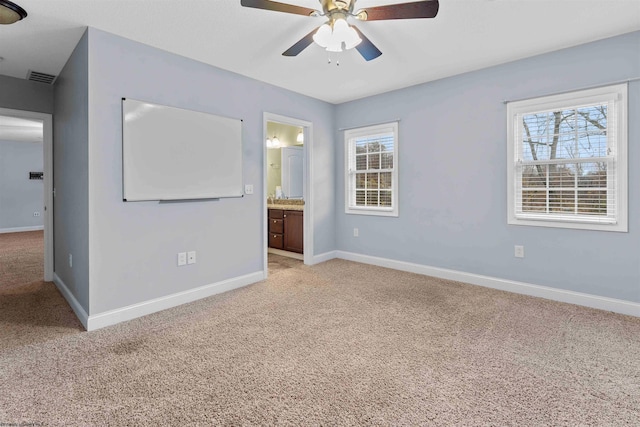 unfurnished bedroom with connected bathroom, multiple windows, light colored carpet, and ceiling fan