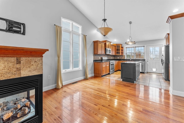 kitchen featuring appliances with stainless steel finishes, hanging light fixtures, a center island, light wood-type flooring, and vaulted ceiling