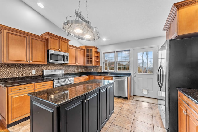 kitchen featuring stainless steel appliances, dark stone countertops, sink, and a center island