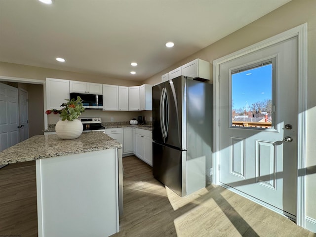 kitchen featuring stainless steel appliances, light hardwood / wood-style floors, a center island, light stone countertops, and white cabinetry