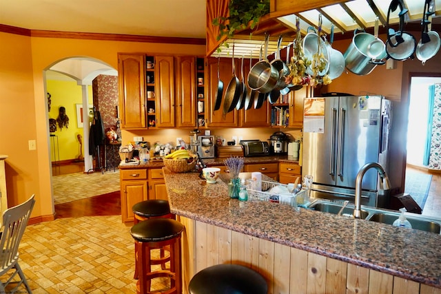 kitchen with high end fridge, kitchen peninsula, sink, ornamental molding, and dark stone countertops