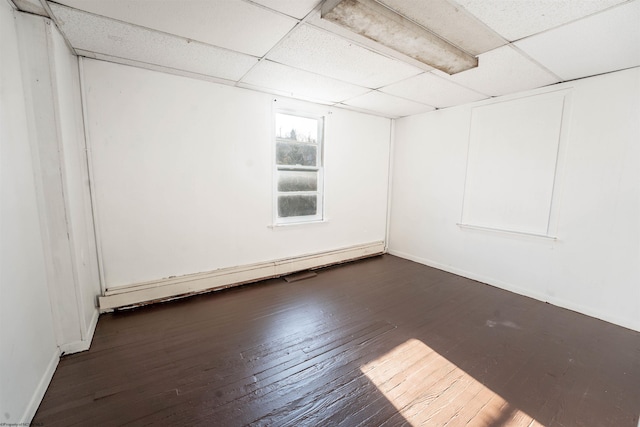 spare room featuring dark wood-type flooring, a drop ceiling, and a baseboard radiator