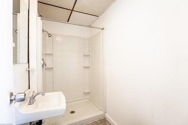 bathroom with walk in shower, a paneled ceiling, and sink