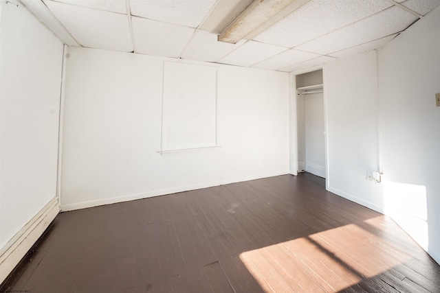 basement featuring baseboard heating, a paneled ceiling, and dark hardwood / wood-style floors